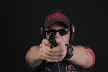 Homem praticando tiro dinâmico de competição com foco em precisão e velocidade.